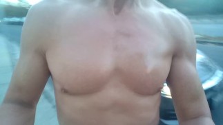 Chico desnudo y musculoso masturbándose frente al tráfico en hora punta